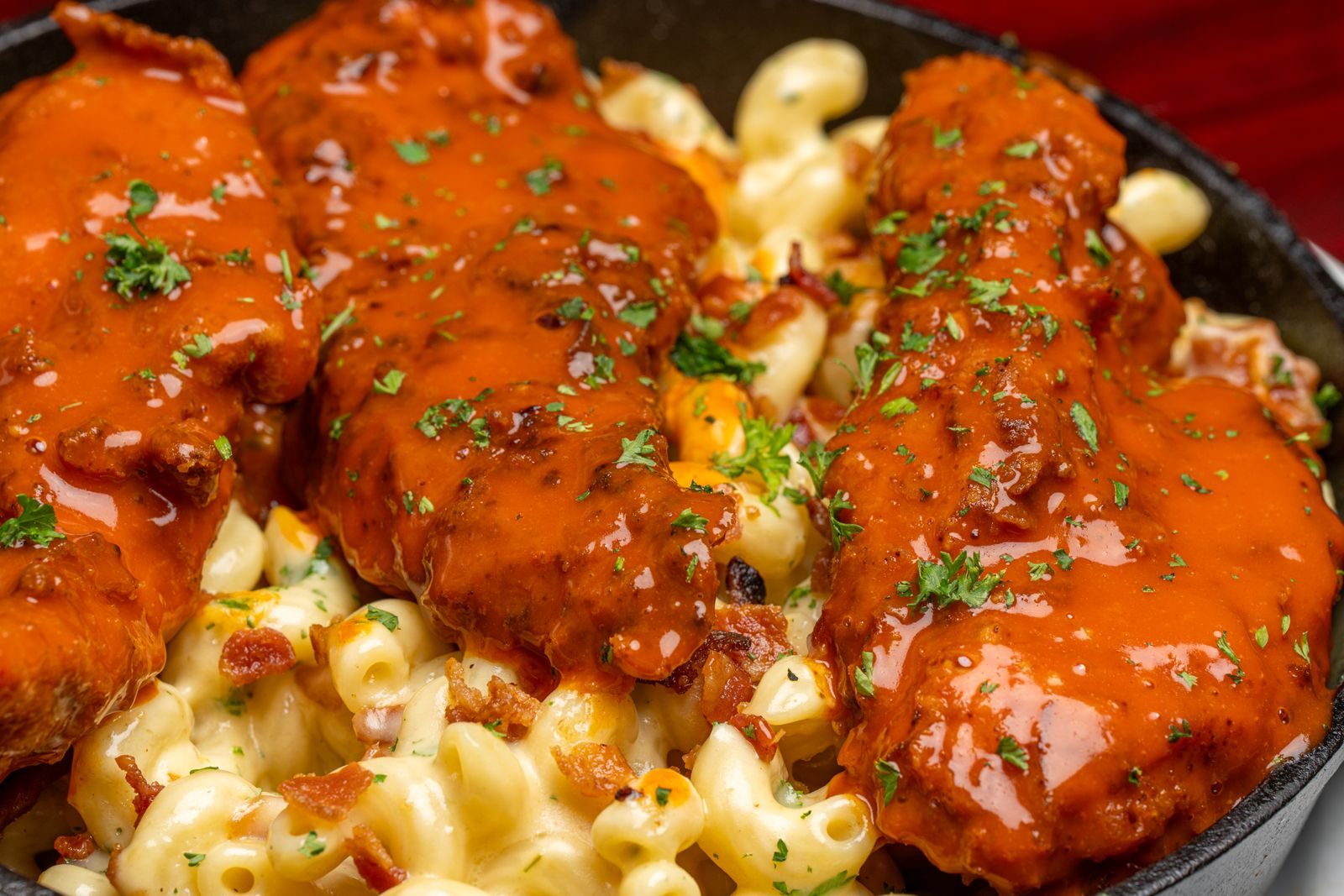 Saucy chicken over creamy baked macaroni and cheese in a cast-iron skillet