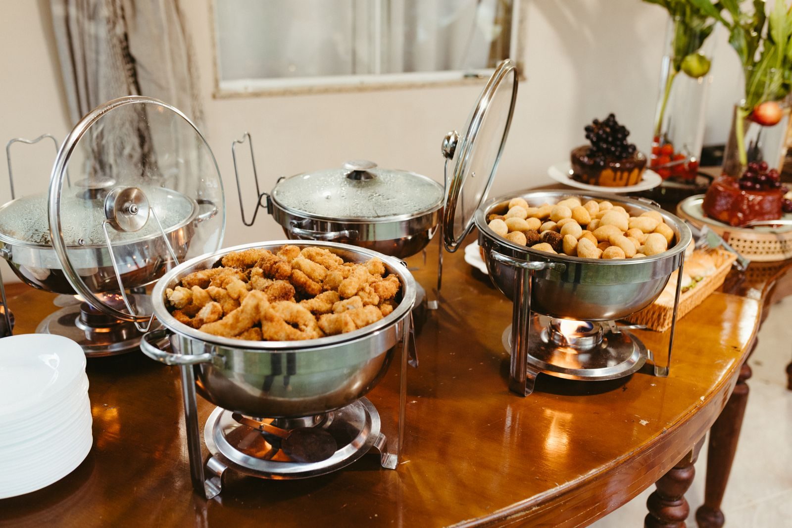A catering buffet of chafing dishes over warmers with stacked service plates