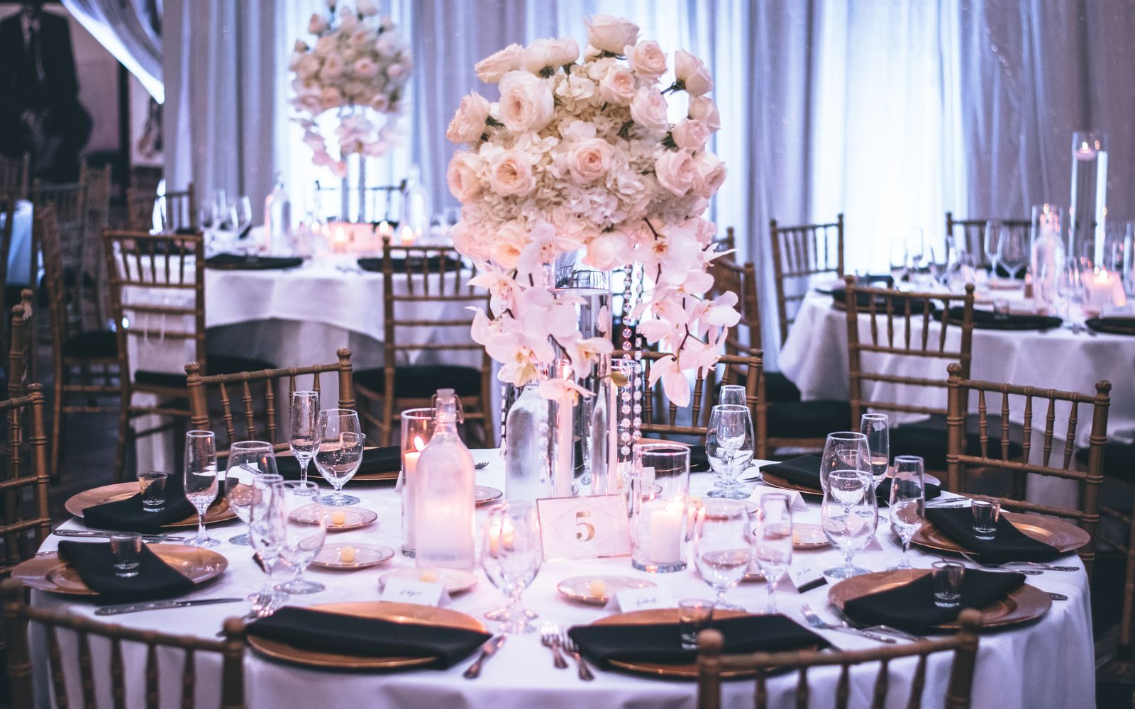 An event table set with a tall floral centerpiece, gold chargers, and candlelight